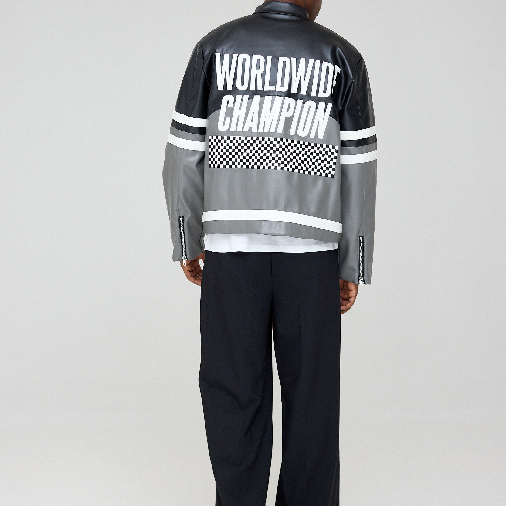 Person wearing a black and gray jacket with 'Worldwide Champion' text on the back, standing against a white background.