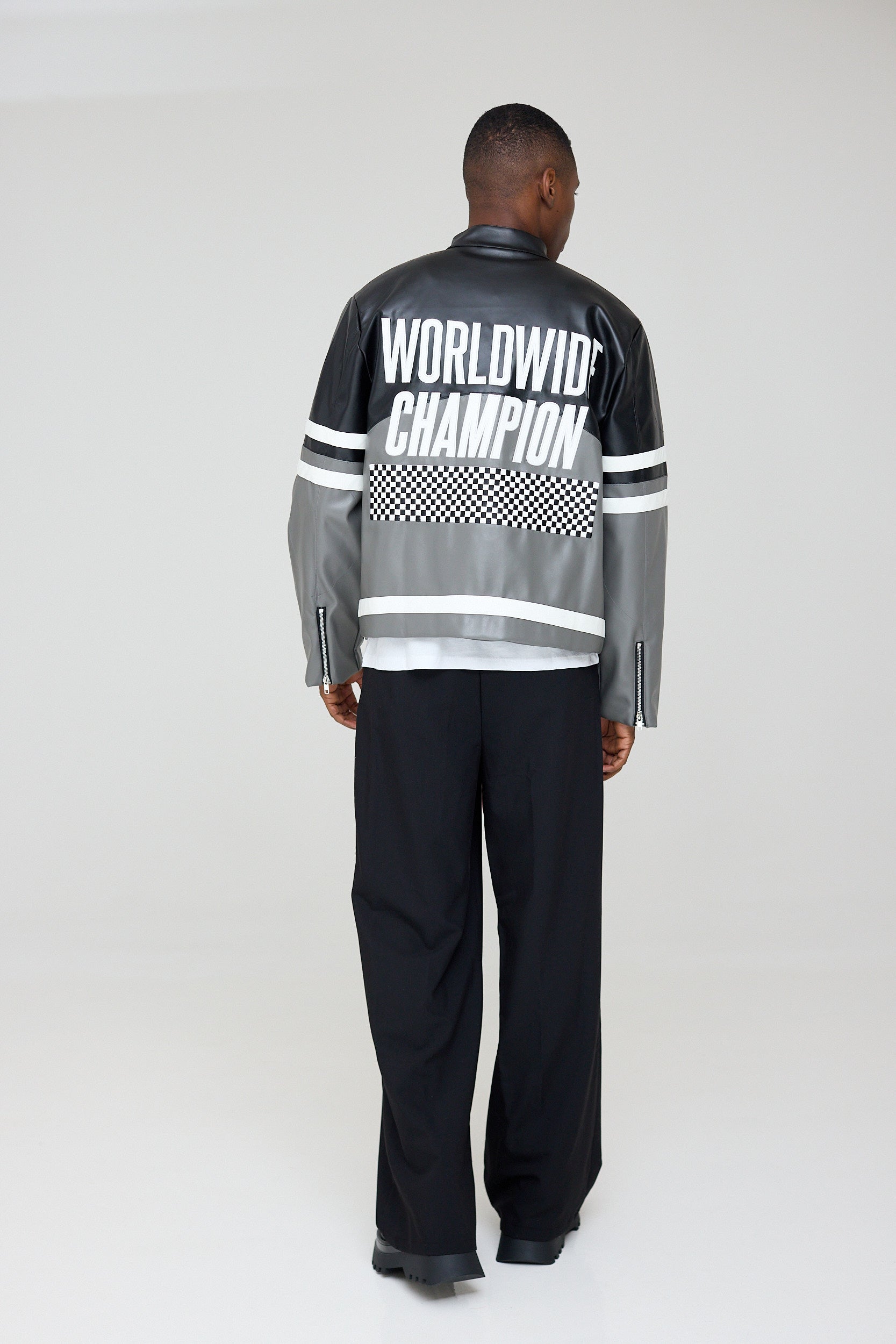 Person wearing a black and gray jacket with 'Worldwide Champion' text on the back, standing against a white background.