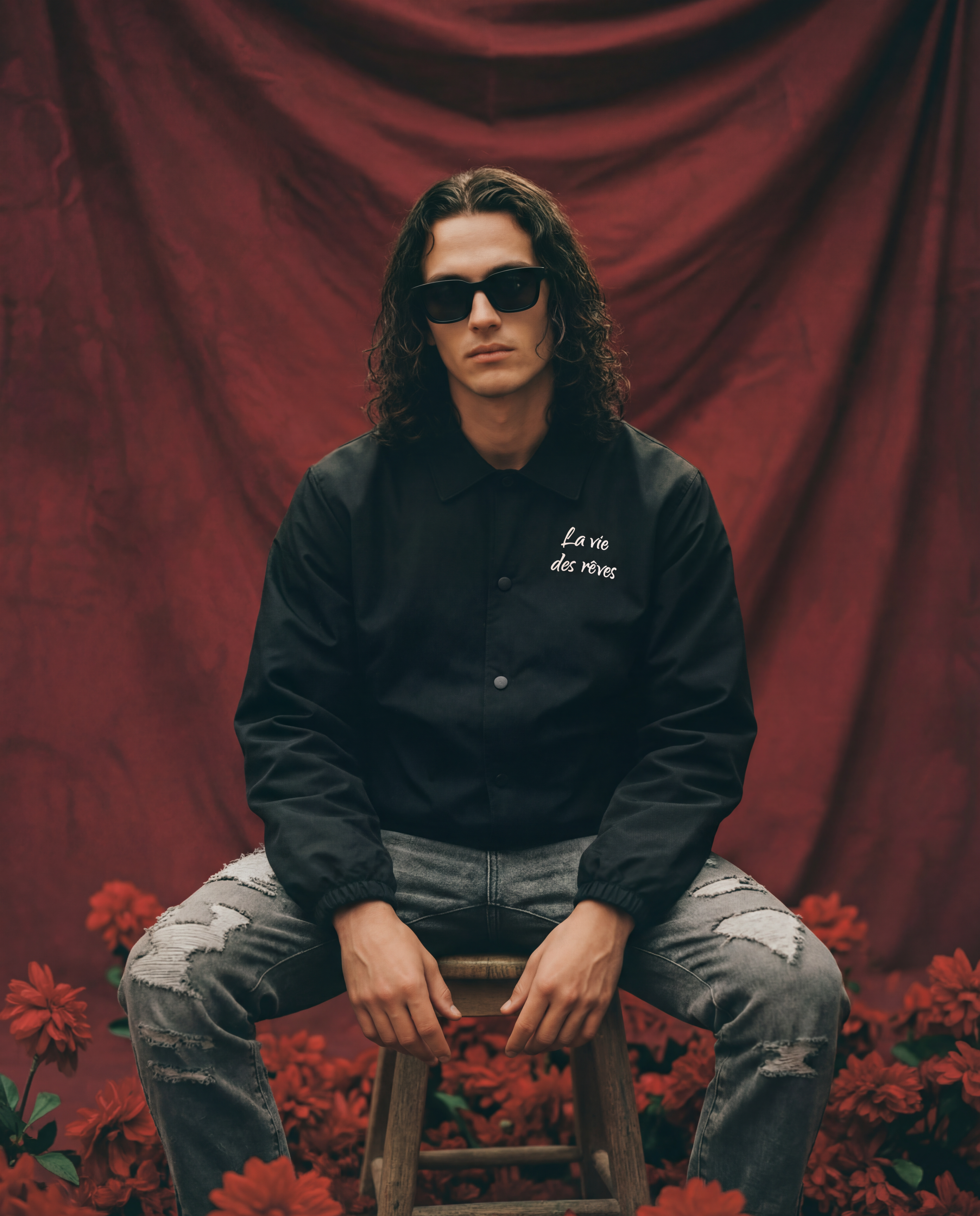 Man wearing sunglasses and a black la vie des reves jacket and grey distressed carpenter jeans.