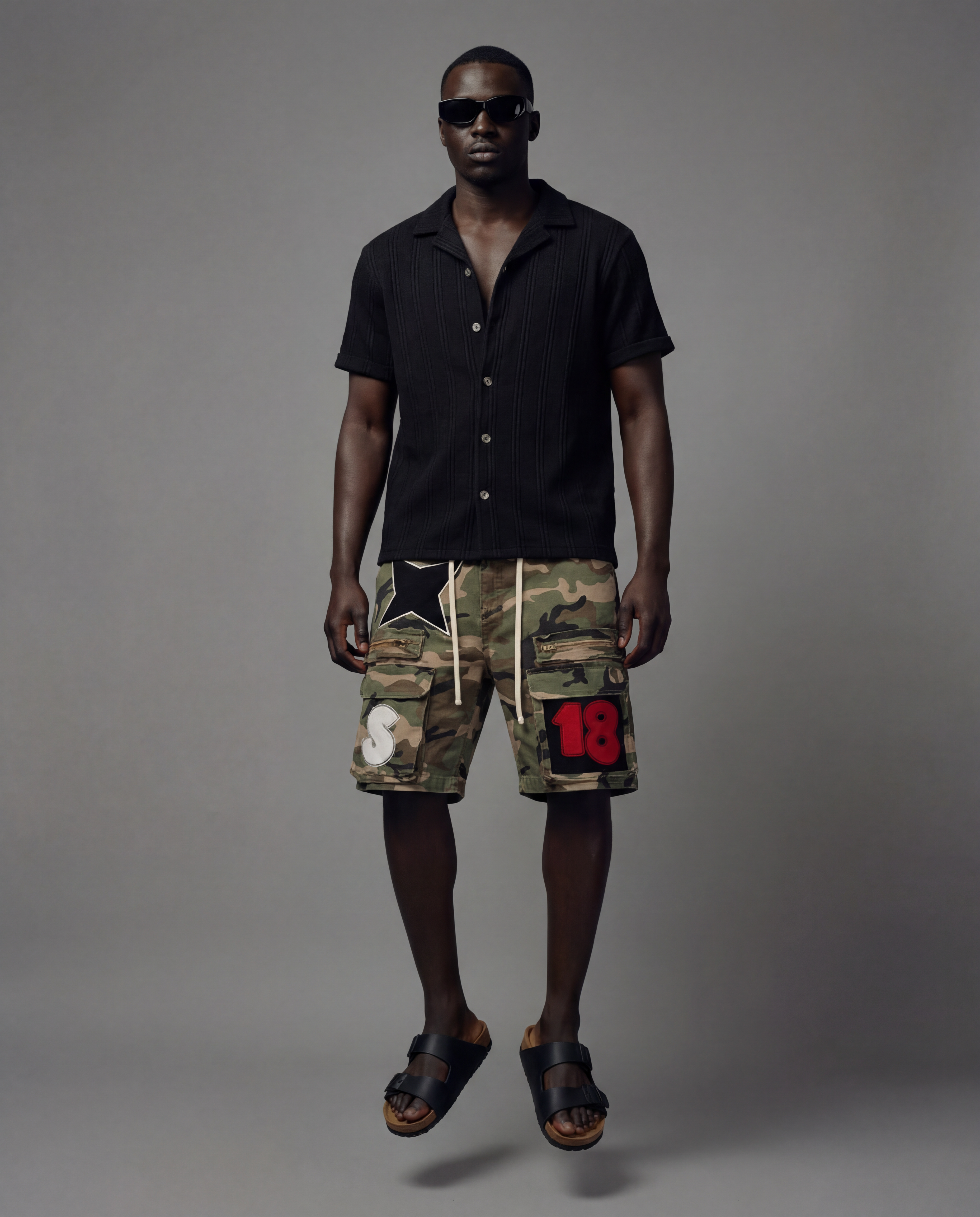 Man wearing a black shirt and camouflage cargo shorts with patches