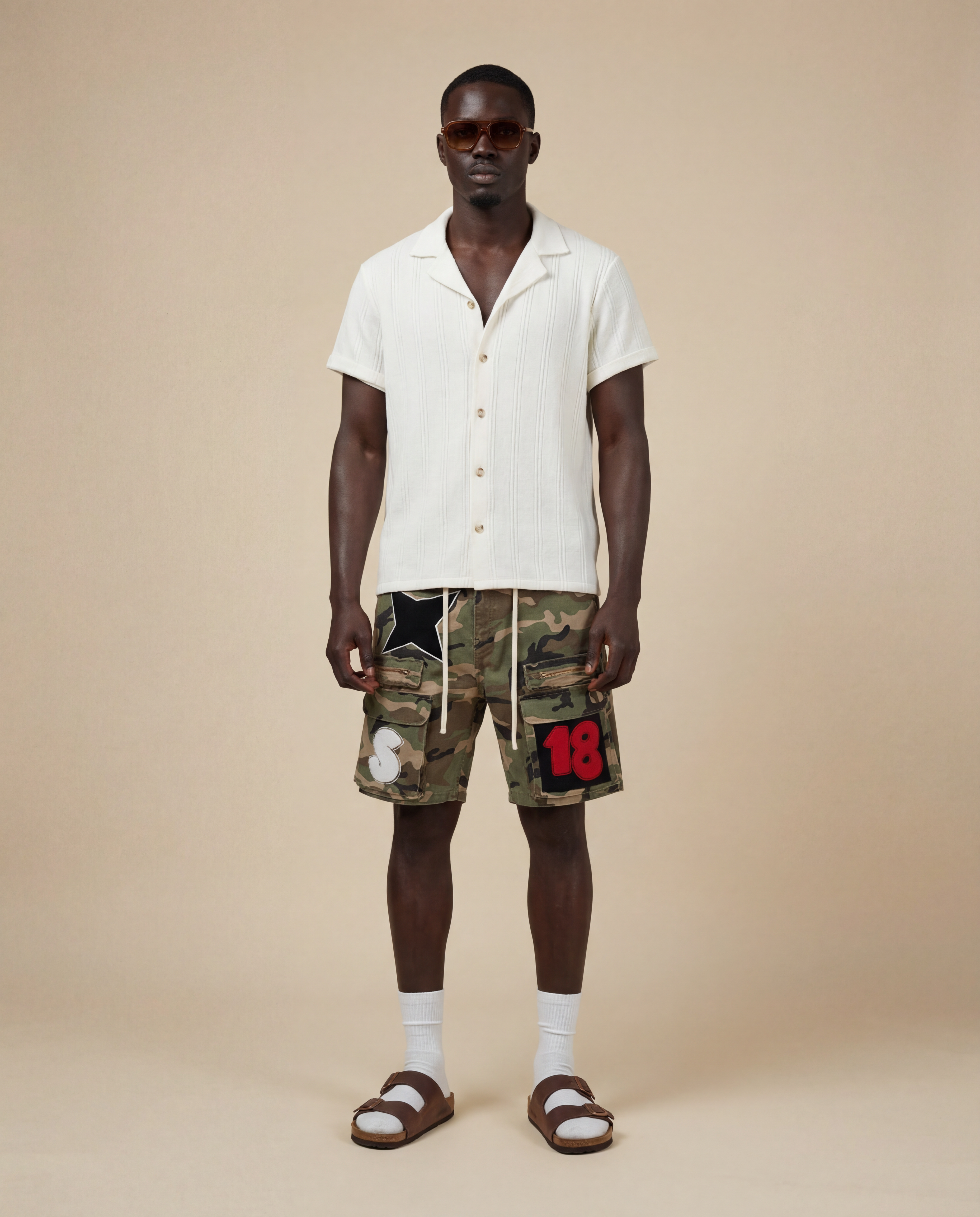 Man wearing a cream shirt and camouflage cargo shorts with patches