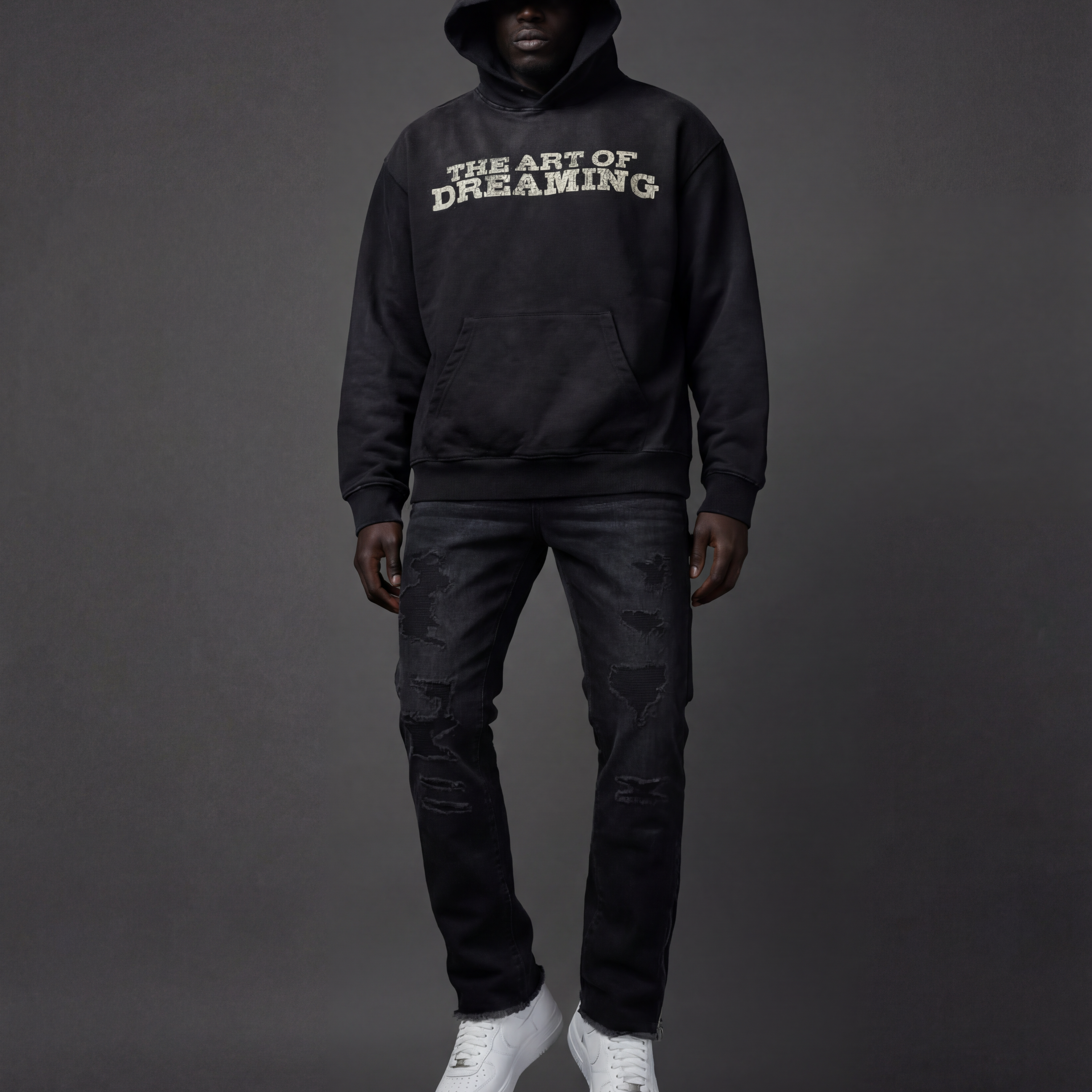 Person wearing a black hoodie with 'The Art of Dreaming' text along with black distressed carpenter.