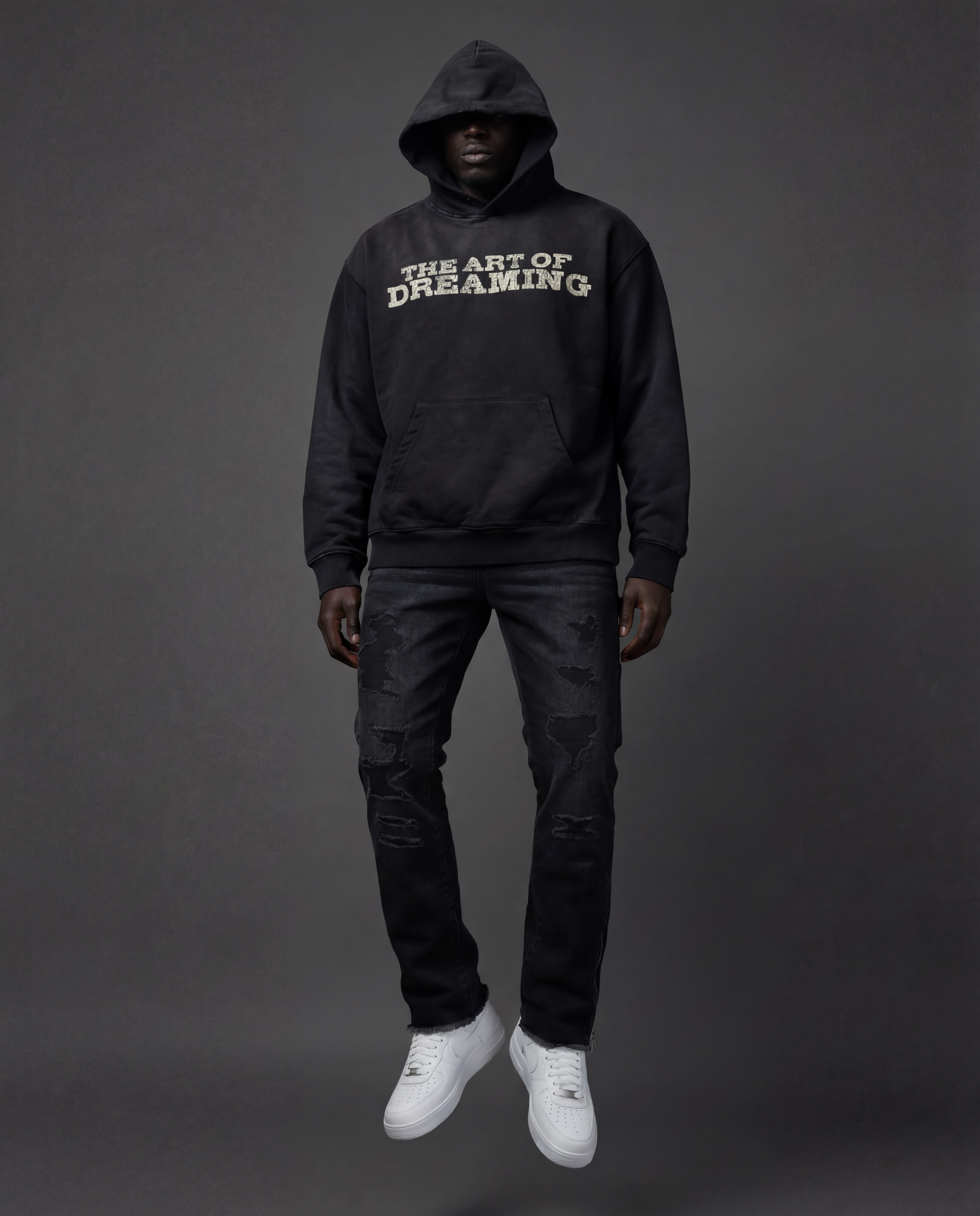 Person wearing a black hoodie with 'The Art of Dreaming' text along with black distressed carpenter.