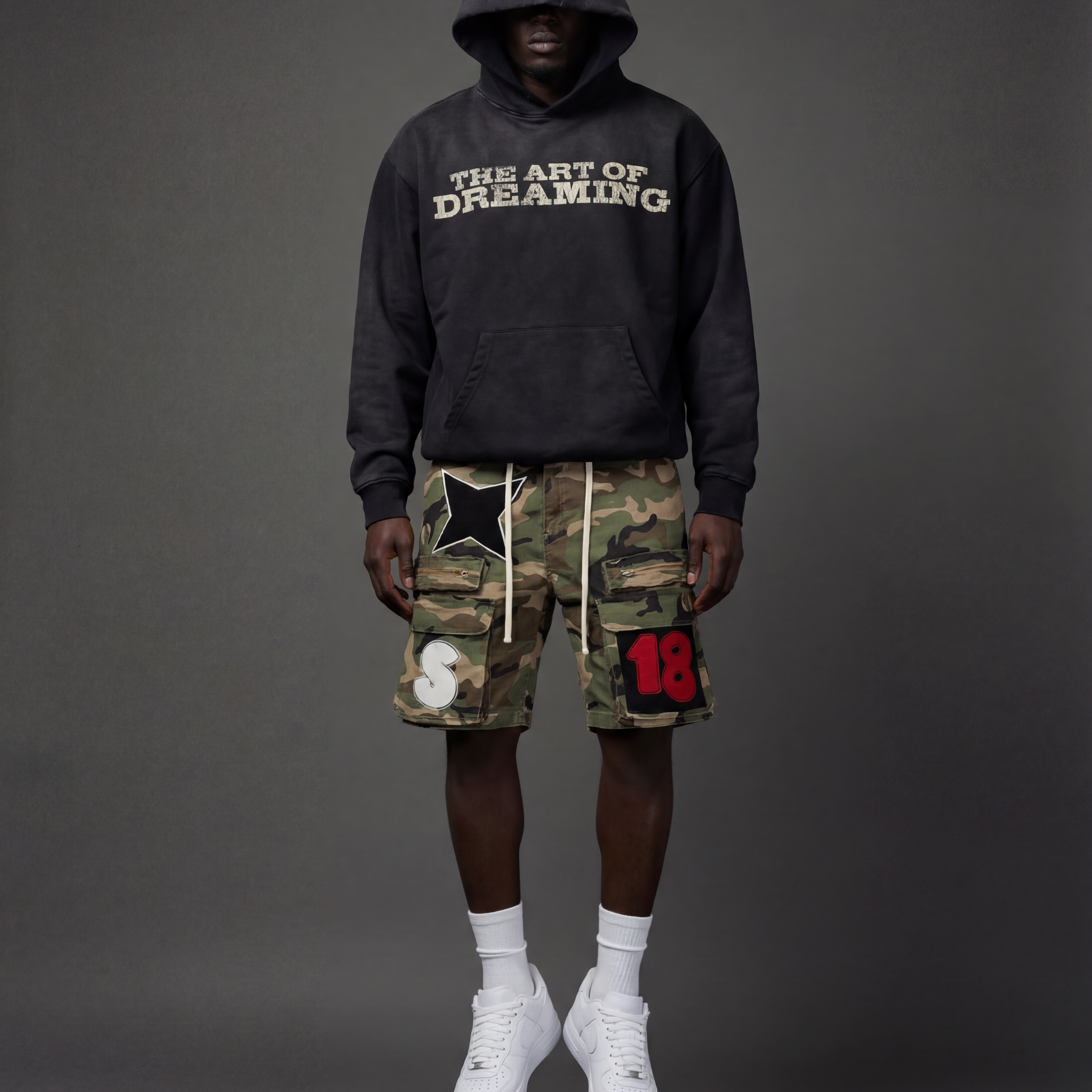 Person wearing a black hoodie with 'The Art of Dreaming' text and camouflage cargo shorts.