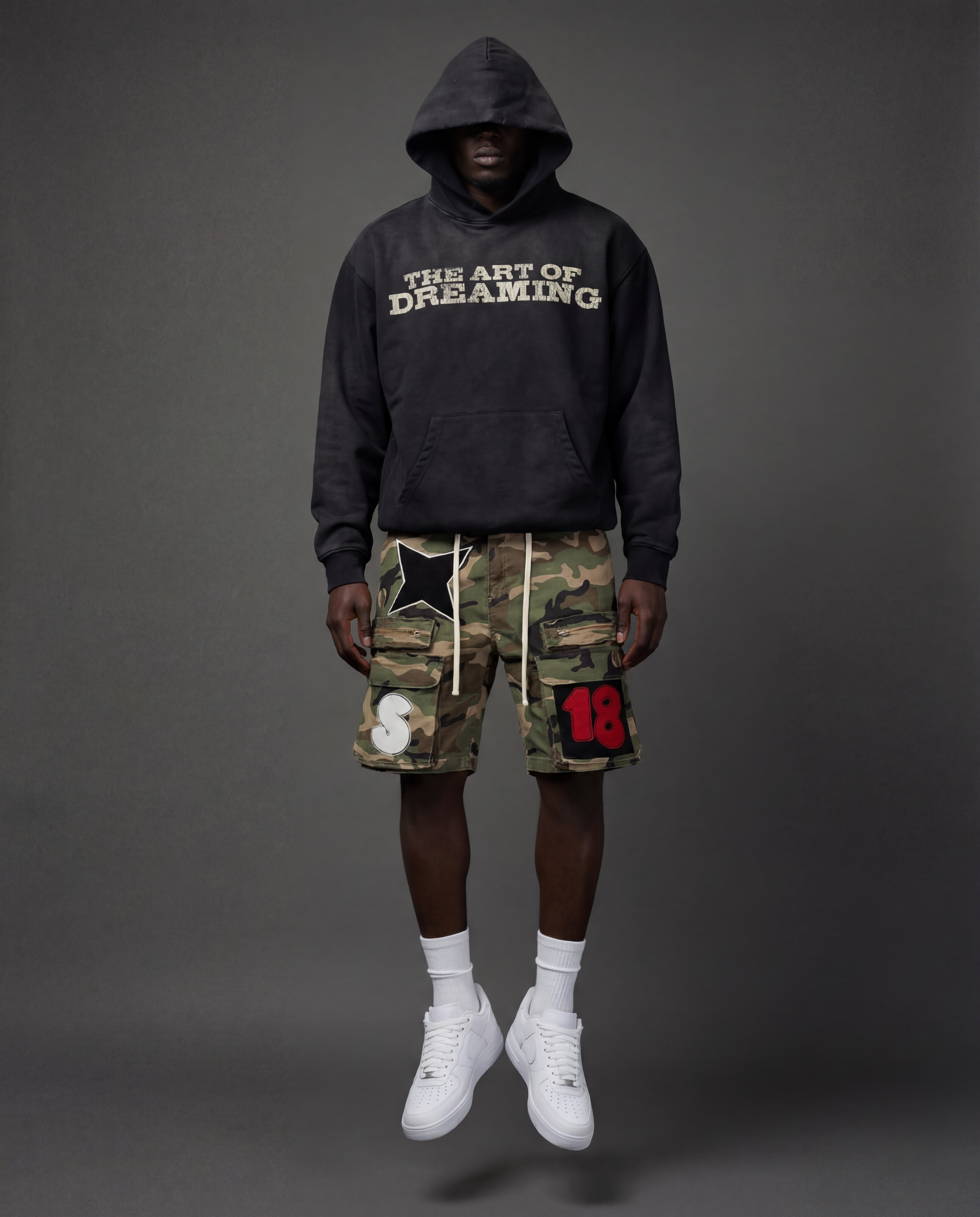 Person wearing a black hoodie with 'The Art of Dreaming' text and camouflage cargo shorts.
