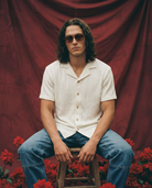 Man sitting wearing a cream knitted shirt with blue carpenter jeans