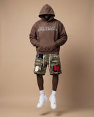 Person wearing a brown hoodie with 'The art of dreaming' text and camouflage cargo shorts.