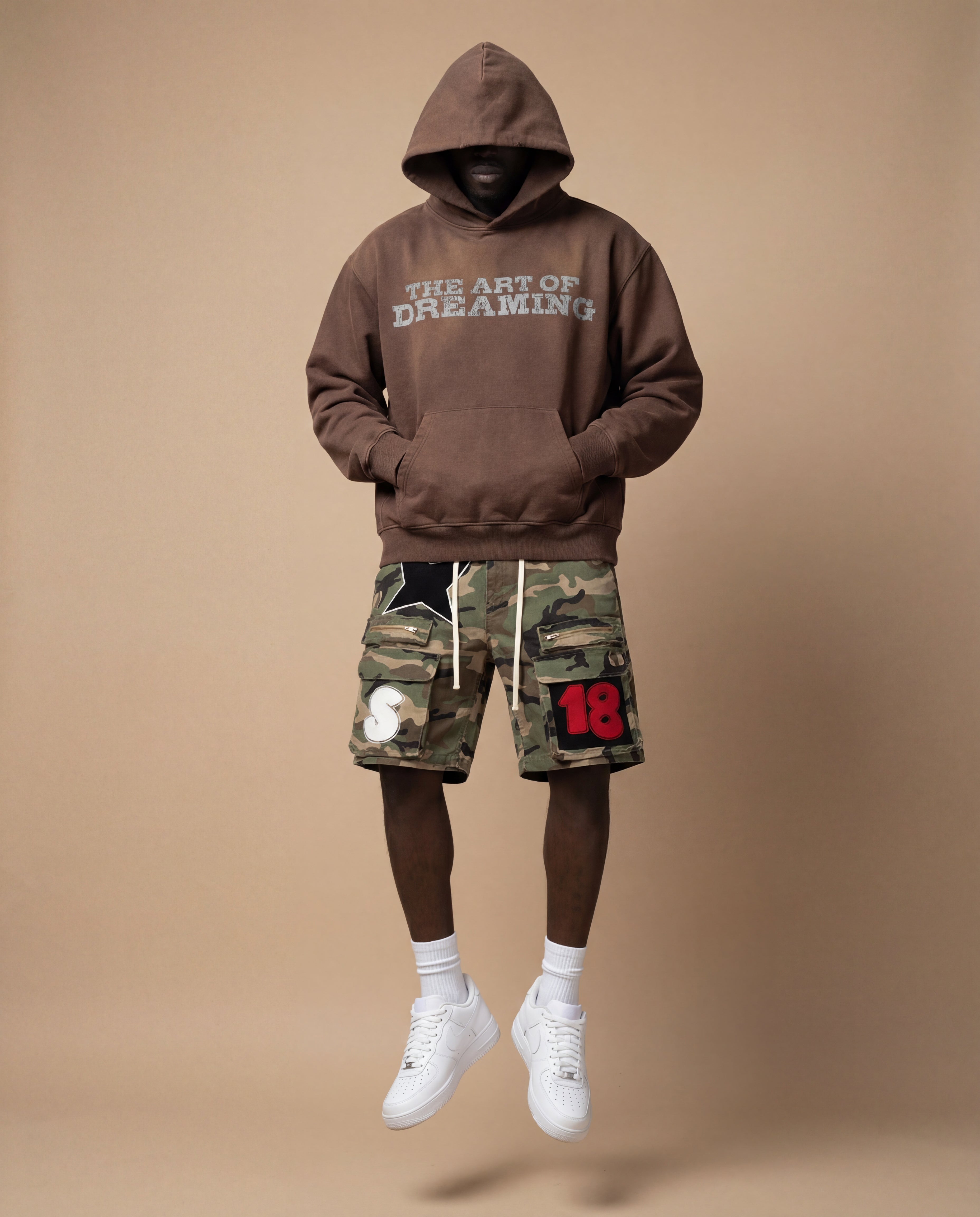 Person wearing a brown hoodie with 'The art of dreaming' text and camouflage cargo shorts.